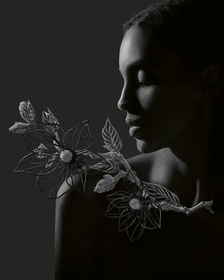 Boucheron, Magnolia necklace, Composition N° 2. Craftsmen scanned a real magnolia tree, including its branches, flowers and buds, to create this aluminium piece. A linear pavé of diamonds makes the aluminium petals covered in black ceramic sparkle, while the centre of the white gold flowers is paved with upside-down diamonds. The stick insect is made of white gold adorned with diamonds. The vase is made from a matte black composite material.